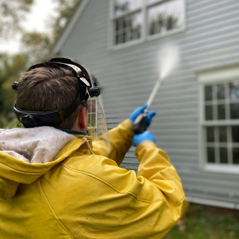 A person pressure washing the side of a house
