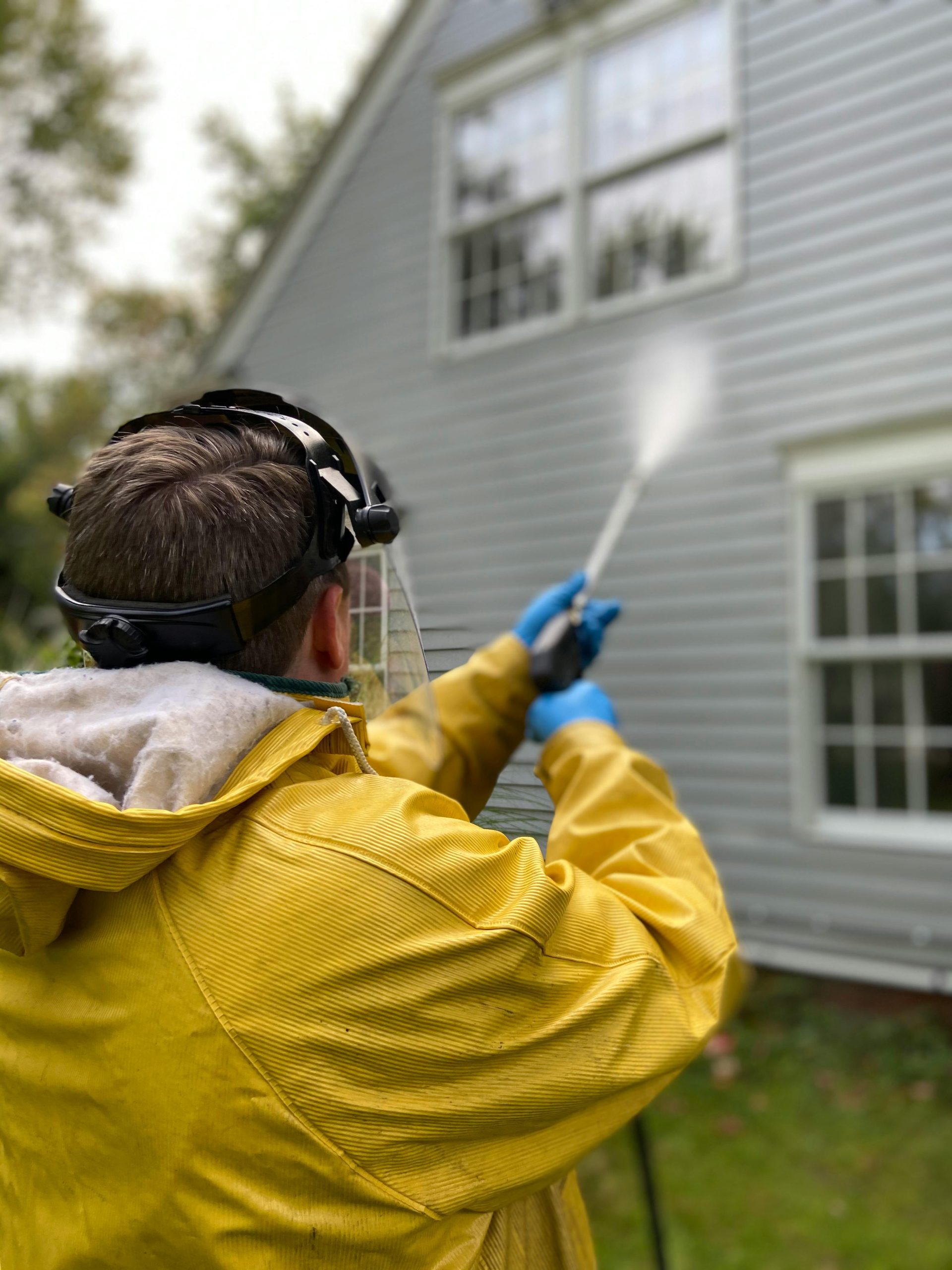 A person pressure washing the side of a house